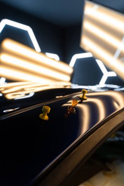 Ağrısız çukur onarma işlemi sırasında LED ışıklarının altındaki çökmüş bir arabanın çatısına birden fazla yapıştırıcı şeridi takılmış. Yapıştırıcı sekmeleri yüzeyi hatasız bir bitiş için hizalamaya ve onarmaya yardımcı olur