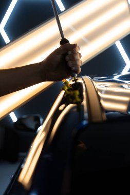 PDR Ayrıntılı yansıma çizgileri kusursuz yüzey restorasyonu için hassas çekme kılavuzu. Ağrısız araba göçüğü teknisyeni, araba gövdesi panellerini onarmak için tutkal şeritlerine sürgülü çekiç kullanıyor.