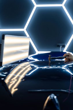 PDR teknisyeni, yapıştırıcı şeritleri ve çekiçle arabanın panelini göçertti. Kontrollü güç, boya hasarı olmadan yüzeyi onarır. Bir PDR sürgülü çekiç yeniden boyanmadan araba göçüğü