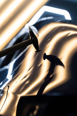 Teknisyen, acısız çukur onarımı sırasında arabanın kaputundaki göçükleri çıkarmak için PDR aletleri kullanıyor. Ağrısız çukur onarma PDR hassasiyet için ışık yansıması altında ezilmeyi içerir.