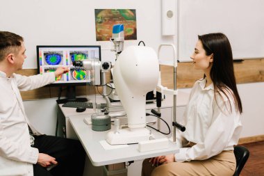 Oftalmolog yarık lambanın yanındaki kız hastaya kornea topografisi gösteriyor. Göz hekimliği kliniğinde korneanın teşhisi ve gözler