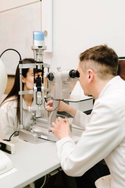 Kesik lambalı bir oftalmolog kadının gözlerini ve korneasını inceliyor. Göz doktoru, göz ve kornea teşhisi koymak için kesik lambadan gelen ışıkla hastanın gözünü aydınlatıyor.