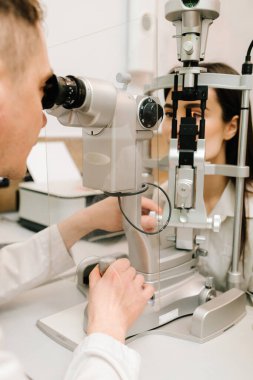 Oftalmolog, göz ve kornea teşhisi koymak için kesik lambadan gelen ışıkla hastanın gözünü aydınlatıyor. Kesik lambalı bir oftalmolog kadının gözlerini ve korneasını inceliyor.