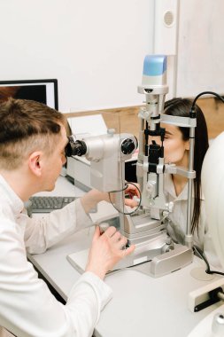 Oftalmolog, göz ve kornea teşhisi koymak için kesik lambadan gelen ışıkla hastanın gözünü aydınlatıyor. Kesik lambalı bir oftalmolog kadının gözlerini ve korneasını inceliyor.