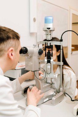 Kesik lambalı bir oftalmolog kadının gözlerini ve korneasını inceliyor. Göz doktoru, göz ve kornea teşhisi koymak için kesik lambadan gelen ışıkla hastanın gözünü aydınlatıyor.