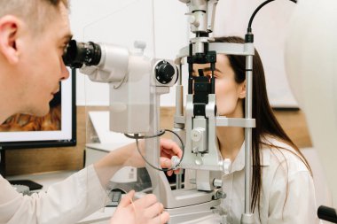 Kesik lambalı bir oftalmolog kadının gözlerini ve korneasını inceliyor. Göz doktoru, göz ve kornea teşhisi koymak için kesik lambadan gelen ışıkla hastanın gözünü aydınlatıyor.