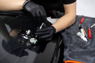 Reçine enjeksiyonuyla ön cam çatlağı onarımı. Teknisyen ön cam enjektörü kullanarak göz çatalını tamir ediyor. Yapısal berraklığı geri getirmek için enjektör uygulaması kullanarak ön camda reçine onarımı