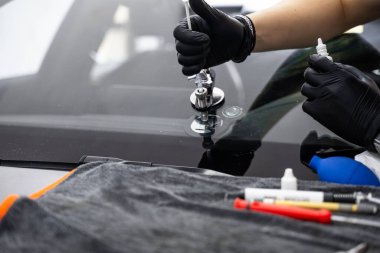 Yapısal berraklığı geri getirmek için enjektör uygulaması kullanarak ön camda reçine onarımı. Reçine enjeksiyonuyla ön cam çatlağı onarımı. Teknisyen ön cam enjektörü kullanarak göz çatalını tamir ediyor.