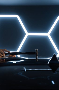 Ağrısız çukur onarma PDR hassasiyet için ışık yansıması altında ezilmeyi içerir. Teknisyen, acısız çukur onarımı sırasında arabanın kaputundaki göçükleri çıkarmak için PDR araçları kullanıyor.