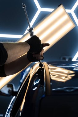 PDR için parlak bir arabanın çatısında çekme aleti kullanmak, basıncı tam olarak ayarlamak. Uzman, metali yeniden boyanmadan eski haline getirmek için ileri çekiş aracı kullanıyor