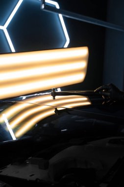 PDR teknisyeni, kaputtaki çukur düzeltmesini kontrol etmek için yansıma lambasına özel bir çekiç tutuyor. Acısız bir araba göçüğü.