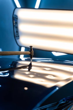 PDR teknisyeni, çarpma aletini ve çekiç kombinasyonunu dolu izlerini düzeltmek için kullanır. Odaklanmış vuruşlar boyaya zarar vermeden metali yeniden hizaladı. Devrilmiş bir aletle kontrol edilen musluklar dolu ile bükülmüş metali yeniden şekillendirir