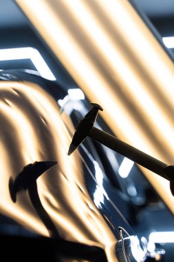 Ağrısız çukur onarma PDR hassasiyet için ışık yansıması altında ezilmeyi içerir. Teknisyen, acısız çukur onarımı sırasında arabanın kaputundaki göçükleri çıkarmak için PDR araçları kullanıyor.