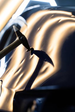 Ağrısız çukur onarma PDR hassasiyet için ışık yansıması altında ezilmeyi içerir. Teknisyen, acısız çukur onarımı sırasında arabanın kaputundaki göçükleri çıkarmak için PDR araçları kullanıyor.
