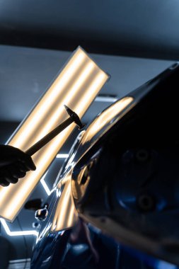 Ağrısız çukur onarma PDR hassasiyet için ışık yansıması altında ezilmeyi içerir. Teknisyen, acısız çukur onarımı sırasında arabanın kaputundaki göçükleri çıkarmak için PDR araçları kullanıyor.