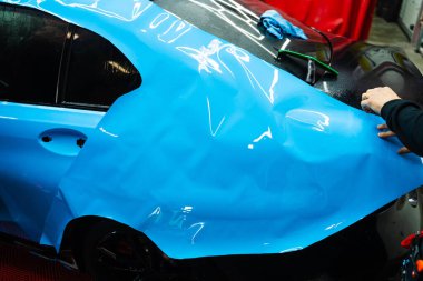 Detaylandırma merkezine kalın mavi vinil ambalaj kurulumu. Detaylar hatları sığdırmak için ustalıkla ambalaj uygular ve pürüzsüz, kusursuz bir paket hizalaması sağlar. Tam ayrıntı sırasında arabaya PPF paketi uygulanıyor