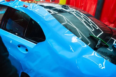 Detaylandırma merkezine kalın mavi vinil ambalaj kurulumu. Detaylar hatları sığdırmak için ustalıkla ambalaj uygular ve pürüzsüz, kusursuz bir paket hizalaması sağlar. Tam ayrıntı sırasında arabaya PPF paketi uygulanıyor