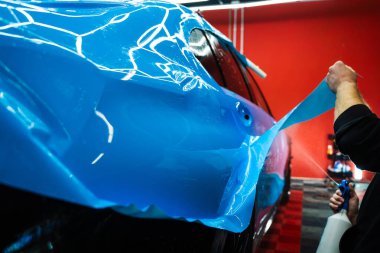 Detaylı uzmanlar mavi PPF filminin kontrollü uygulaması için hidrasyon spreyi kullanırlar. Detaylayıcı mükemmel, kabarcıksız hizalama için canlı mavi vinil sarma uygulamak için sprey destekli yöntem kullanır