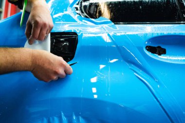 Mavi PPF 'yi bıçakla kesiyorum. Detaylı iş sırasında mavi boya koruma filmini bıçakla kesmek hassas kenarlar sağlar. Detaylı teknisyen mükemmel kontur için bir araba paneli üzerindeki mavi PPF buduyor