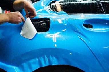 Mavi PPF 'yi bıçakla kesiyorum. Detaylı iş sırasında mavi boya koruma filmini bıçakla kesmek hassas kenarlar sağlar. Detaylı teknisyen mükemmel kontur için bir araba paneli üzerindeki mavi PPF buduyor