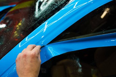 Mavi PPF 'yi bıçakla kesiyorum. Detaylı iş sırasında mavi boya koruma filmini bıçakla kesmek hassas kenarlar sağlar. Detaylı teknisyen mükemmel kontur için bir araba paneli üzerindeki mavi PPF buduyor