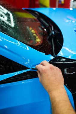 Detaylı iş sırasında mavi boya koruma filmini bıçakla kesmek hassas kenarlar sağlar. Detaylı teknisyen mavi PPF 'yi mükemmel bir kondisyon için bir araç paneline yerleştirdi. Bıçakla mavi PPF kesiliyor
