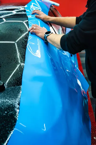 Tüm detaylar sırasında arabaya PPF ambalajı uygulanıyor. Detaylandırma merkezine kalın mavi vinil ambalaj kurulumu. Detaylar hatları sığdırmak için ustalıkla paket uygular ve pürüzsüz, pürüzsüz paket hizalamasını sağlar