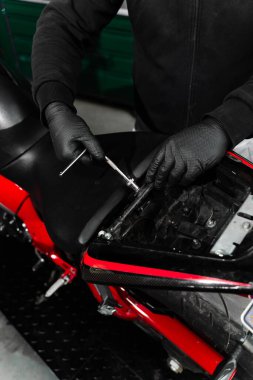 Teknisyen, teşhis için iç bileşenlere ulaşmak için aletleri kullanarak motosiklet koltuğunu dikkatlice kaldırıyor. Motosiklet koltuğunu kaldırmak elektrik sistemini incelemek için gereklidir.