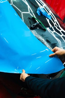 Tüm detaylar sırasında arabaya PPF ambalajı uygulanıyor. Detaylandırma merkezine kalın mavi vinil ambalaj kurulumu. Detaylar hatları sığdırmak için ustalıkla paket uygular ve pürüzsüz, pürüzsüz paket hizalamasını sağlar