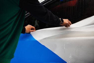 Detaylı merkezdeki araç paneline ıslak plazma yapıştırma. Araba yüzeyini çizik ve ultraviyole ışınlardan korumak için PPF paketleme sırasında koruyucu film katmanı
