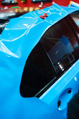 Detaylar hatları sığdırmak için ustalıkla ambalaj uygular ve pürüzsüz, kusursuz bir paket hizalaması sağlar. Tüm detaylar sırasında arabaya PPF ambalajı uygulanıyor. Ayrıntılı merkeze kalın mavi vinil paket kurulumu