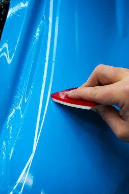 Kırmızı bir cam sileceği kullanarak yüksek parlak mavi bir PPF uygulamak, arabanın baloncuksuz ve pürüzsüz bir yüzeyi olmasını sağlar. Mavi PPF, kırmızı cam sileceği ile arabayı temizlerken uygulanır ve hasarı engeller