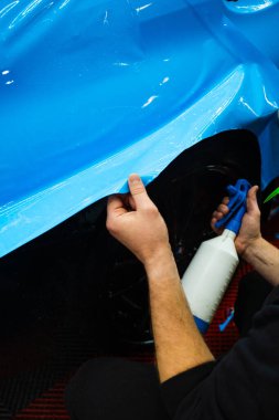 Detaylı uzmanlar mavi PPF filminin kontrollü uygulaması için hidrasyon spreyi kullanırlar. Detaylayıcı mükemmel, kabarcıksız hizalama için canlı mavi vinil sarma uygulamak için sprey destekli yöntem kullanır