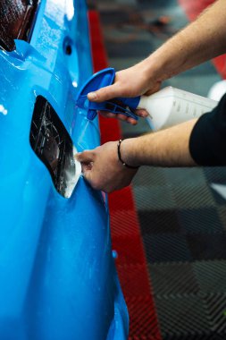 Detaylı uzmanlar mavi PPF filminin kontrollü uygulaması için hidrasyon spreyi kullanırlar. Detaylayıcı mükemmel, kabarcıksız hizalama için canlı mavi vinil sarma uygulamak için sprey destekli yöntem kullanır