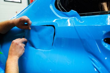 Mavi PPF 'yi bıçakla kesiyorum. Detaylı iş sırasında mavi boya koruma filmini bıçakla kesmek hassas kenarlar sağlar. Detaylı teknisyen mükemmel kontur için bir araba paneli üzerindeki mavi PPF buduyor