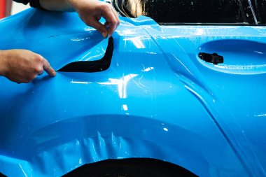 Mavi PPF 'yi bıçakla kesiyorum. Detaylı iş sırasında mavi boya koruma filmini bıçakla kesmek hassas kenarlar sağlar. Detaylı teknisyen mükemmel kontur için bir araba paneli üzerindeki mavi PPF buduyor