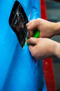 Mavi PPF, yeşil cam sileceği ile arabayı temizlerken ve hasarı engellemek için uygulanmış. Yeşil bir cam sileceği kullanarak yüksek parlak mavi bir PPF uygulamak, arabanın baloncuksuz ve pürüzsüz bir yüzey sağlamasını sağlar