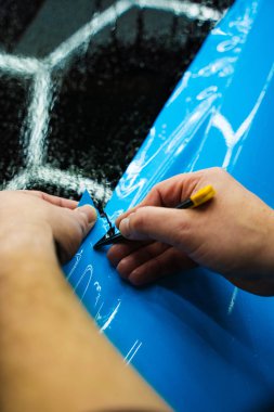 Detaylı teknisyen mavi PPF 'yi mükemmel bir kondisyon için bir araç paneline yerleştirdi. Mavi PPF 'yi bıçakla kesiyorum. Detaylı iş sırasında mavi boya koruma filminin bıçakla kesilmesi hassas kenarları sağlar..