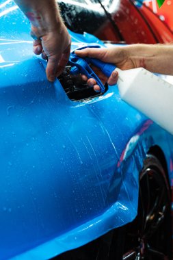 Detaylar, köpüksüz hizalama için canlı mavi vinil ambalaj uygulamak için sprey destekli metot kullanır. Detaylı uzmanlar mavi PPF filminin kontrollü uygulaması için hidrasyon spreyi kullanırlar