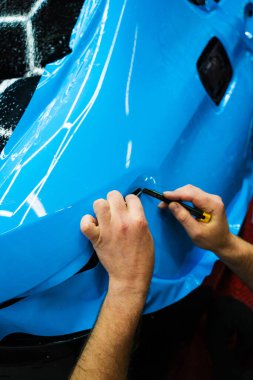Detaylı teknisyen mavi PPF 'yi mükemmel bir kondisyon için bir araç paneline yerleştirdi. Mavi PPF 'yi bıçakla kesiyorum. Detaylı iş sırasında mavi boya koruma filminin bıçakla kesilmesi hassas kenarları sağlar..