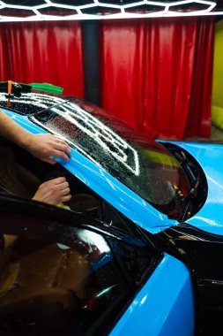 Detaylar, köpüksüz hizalama için canlı mavi vinil ambalaj uygulamak için sprey destekli metot kullanır. Detaylı uzmanlar mavi PPF filminin kontrollü uygulaması için hidrasyon spreyi kullanırlar