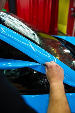 Detaylı teknisyen mavi PPF 'yi mükemmel bir kondisyon için bir araç paneline yerleştirdi. Mavi PPF 'yi bıçakla kesiyorum. Detaylı iş sırasında mavi boya koruma filminin bıçakla kesilmesi hassas kenarları sağlar..