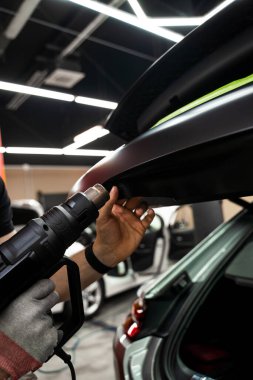 Araba plastiği. Isı tabancasıyla sarılıyor. Isı tabancasıyla arabaya siyah vinil ambalaj uygulamak kesin yapışmayı ve kusursuz yüzey kaplamasını sağlar. Vinil ambalaj için kullanılan ısı silahı yapıştırıcıyı etkinleştirir.