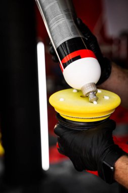 Sarı parlatma yastığına bileşik uygulanıyor. Araba temizliği ve boya düzeltme hazırlığı. Cilalama bileşimi sarı köpük pede eşit olarak uygulanır, kusursuz boya düzeltmesi için yüzeyi hazırlar.