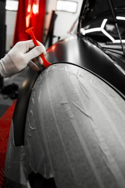 Bir araba paneli kenarına mat siyah sargı uygulamak için kırpma aracı. Trim Tool 'la araba sarma. Araç temizleme, pürüzsüz bitiş için plastik takoz aracı kullanılarak budanma etrafına vinil sarma uygular