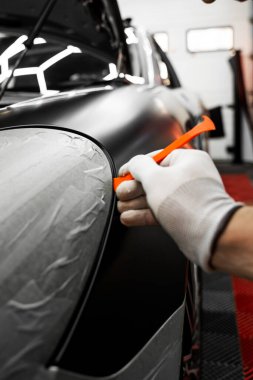 Bir araba paneli kenarına mat siyah sargı uygulamak için kırpma aracı. Trim Tool 'la araba sarma. Araç temizleme, pürüzsüz bitiş için plastik takoz aracı kullanılarak budanma etrafına vinil sarma uygular