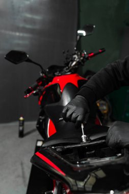 Teknisyen, teşhis için iç bileşenlere ulaşmak için aletleri kullanarak motosiklet koltuğunu dikkatlice kaldırıyor. Motosiklet koltuğunu kaldırmak elektrik sistemini incelemek için gereklidir.