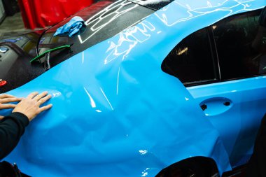 Tüm detaylar sırasında arabaya PPF ambalajı uygulanıyor. Detaylandırma merkezine kalın mavi vinil ambalaj kurulumu. Detaylar hatları sığdırmak için ustalıkla paket uygular ve pürüzsüz, pürüzsüz paket hizalamasını sağlar