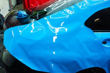 Tüm detaylar sırasında arabaya PPF ambalajı uygulanıyor. Detaylandırma merkezine kalın mavi vinil ambalaj kurulumu. Detaylar hatları sığdırmak için ustalıkla paket uygular ve pürüzsüz, pürüzsüz paket hizalamasını sağlar