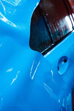 Detaylandırma merkezine kalın mavi vinil ambalaj kurulumu. Detaylar hatları sığdırmak için ustalıkla ambalaj uygular ve pürüzsüz, kusursuz bir paket hizalaması sağlar. Tam ayrıntı sırasında arabaya PPF paketi uygulanıyor